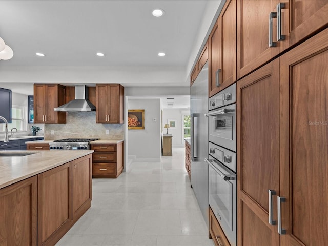 kitchen with wall chimney exhaust hood, light tile patterned flooring, tasteful backsplash, sink, and stainless steel appliances