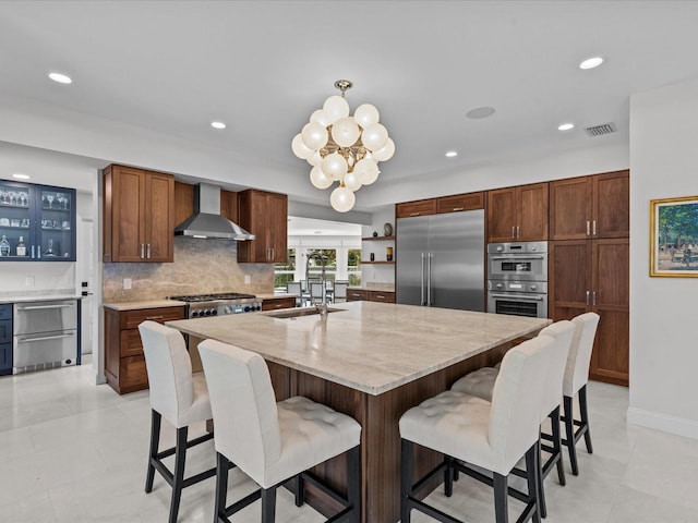 kitchen featuring wall chimney range hood, a kitchen island with sink, tasteful backsplash, sink, and stainless steel appliances