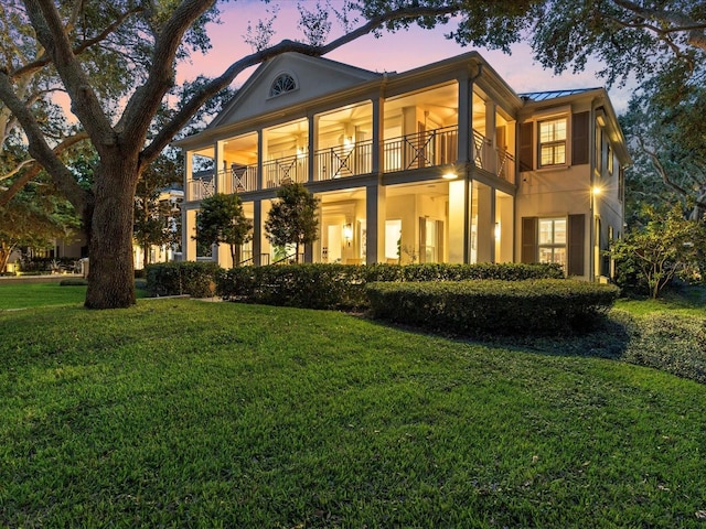 back house at dusk with a balcony and a lawn