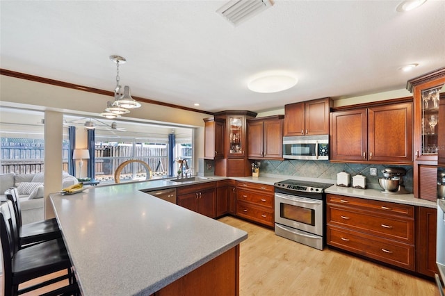 kitchen featuring hanging light fixtures, light hardwood / wood-style floors, stainless steel appliances, crown molding, and a kitchen bar