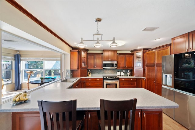 kitchen with decorative light fixtures, stainless steel appliances, sink, and a kitchen breakfast bar