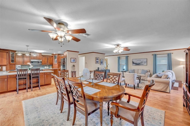 dining area with light wood-style flooring, a textured ceiling, visible vents, ceiling fan, and ornamental molding