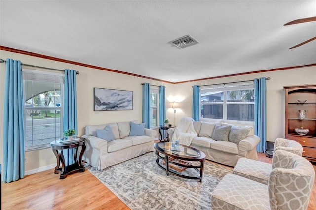 living room with wood finished floors, ceiling fan, baseboards, ornamental molding, and visible vents