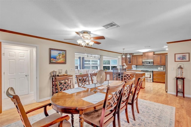 dining space featuring light wood-type flooring, visible vents, crown molding, and ceiling fan