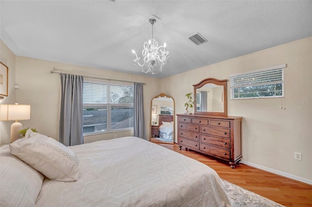 bedroom with baseboards, a notable chandelier, wood finished floors, and visible vents