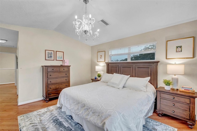 bedroom featuring lofted ceiling, visible vents, light wood finished floors, and a notable chandelier