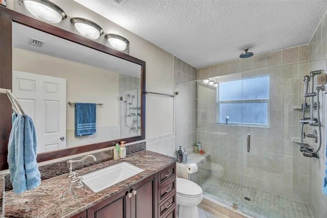 bathroom with a textured ceiling, toilet, visible vents, a shower stall, and vanity