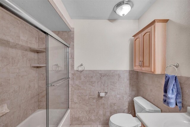 bathroom featuring tile walls, vanity, toilet, and bath / shower combo with glass door