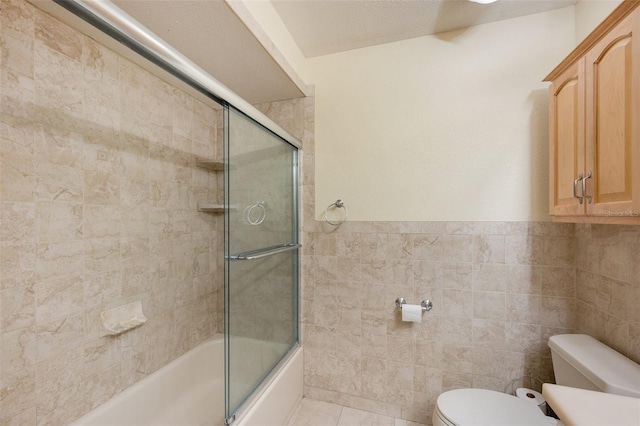 full bath featuring tile walls, a wainscoted wall, toilet, tile patterned flooring, and shower / bath combination with glass door