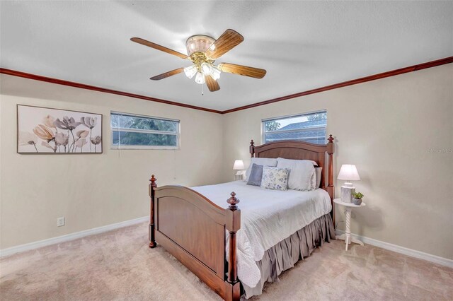 bedroom with light colored carpet, ceiling fan, baseboards, and crown molding