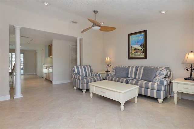 tiled living room with a textured ceiling, ornate columns, and ceiling fan