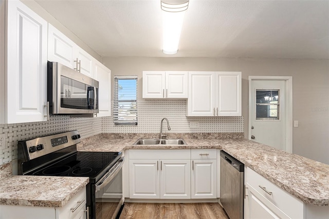 kitchen with kitchen peninsula, sink, white cabinetry, light wood-type flooring, and appliances with stainless steel finishes