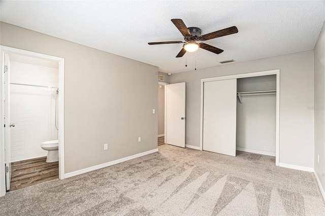 unfurnished bedroom featuring ensuite bathroom, ceiling fan, a textured ceiling, light colored carpet, and a closet