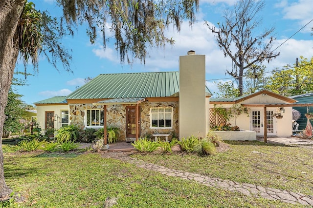 view of front facade featuring metal roof, stone siding, french doors, a chimney, and a front yard