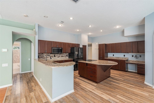 kitchen with a kitchen island, light stone countertops, dark brown cabinetry, refrigerator with ice dispenser, and light hardwood / wood-style flooring