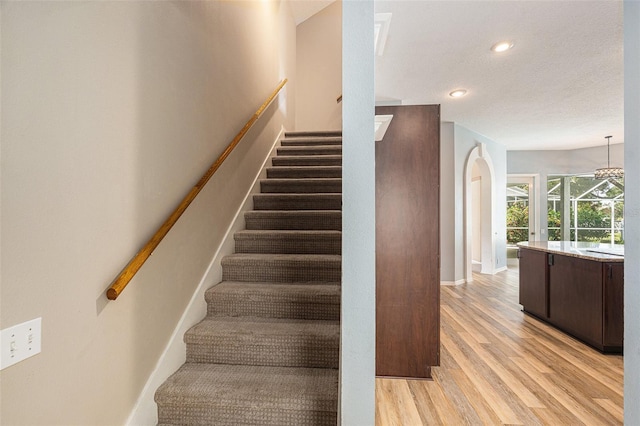 stairway with a notable chandelier, hardwood / wood-style flooring, and a textured ceiling