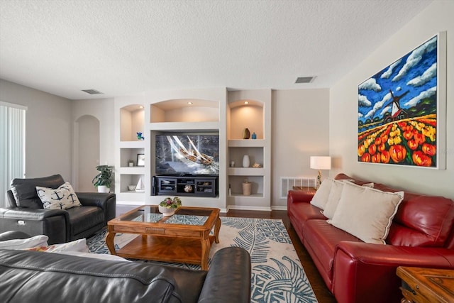 living room featuring a textured ceiling, built in shelves, and hardwood / wood-style floors