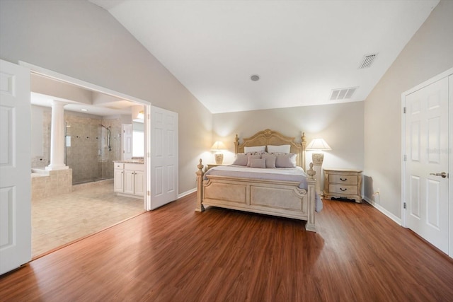 bedroom featuring ensuite bath, decorative columns, vaulted ceiling, and hardwood / wood-style flooring