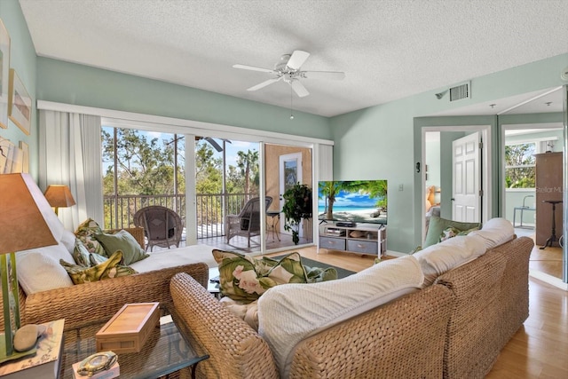 living room featuring a textured ceiling, light wood-type flooring, and ceiling fan