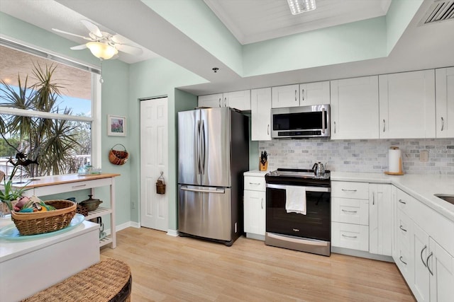 kitchen with white cabinets, stainless steel appliances, light wood-type flooring, and tasteful backsplash