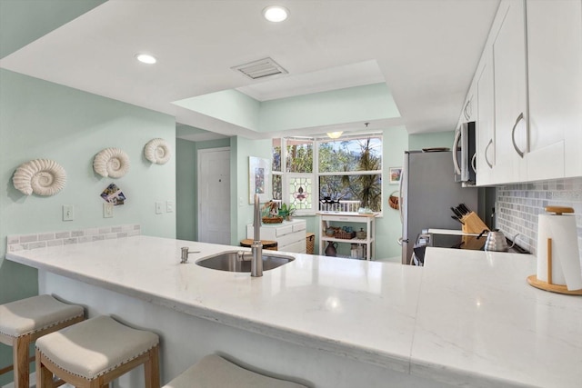 kitchen with tasteful backsplash, sink, kitchen peninsula, white cabinetry, and a breakfast bar area