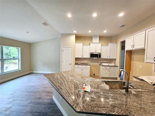 kitchen with dark stone counters, a center island, tasteful backsplash, sink, and white cabinetry