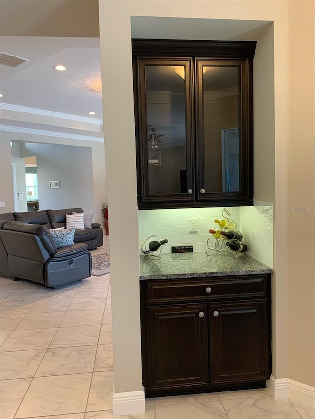 bar with light stone counters, crown molding, tasteful backsplash, and dark brown cabinetry