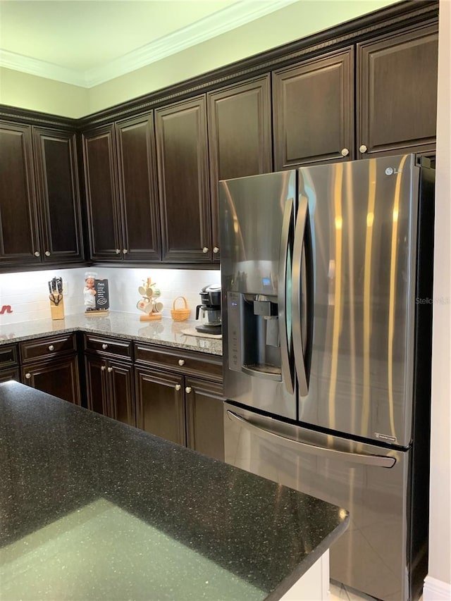 kitchen with stainless steel refrigerator with ice dispenser, dark stone counters, crown molding, and dark brown cabinets
