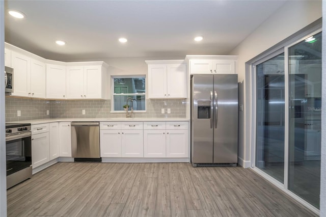 kitchen featuring appliances with stainless steel finishes, white cabinetry, light hardwood / wood-style floors, and tasteful backsplash