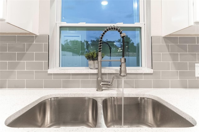 interior details featuring white cabinets, tasteful backsplash, sink, and light stone countertops