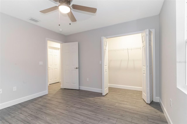 unfurnished bedroom featuring light hardwood / wood-style floors, a closet, a spacious closet, and ceiling fan