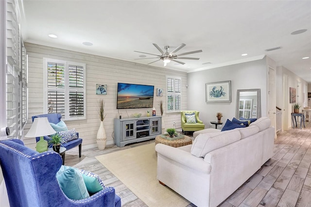 living room with ceiling fan, wooden walls, crown molding, and light hardwood / wood-style floors