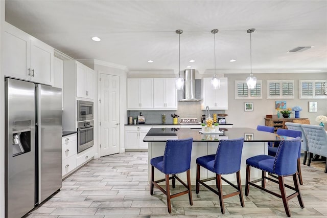 kitchen featuring appliances with stainless steel finishes, a kitchen breakfast bar, white cabinetry, wall chimney exhaust hood, and decorative light fixtures