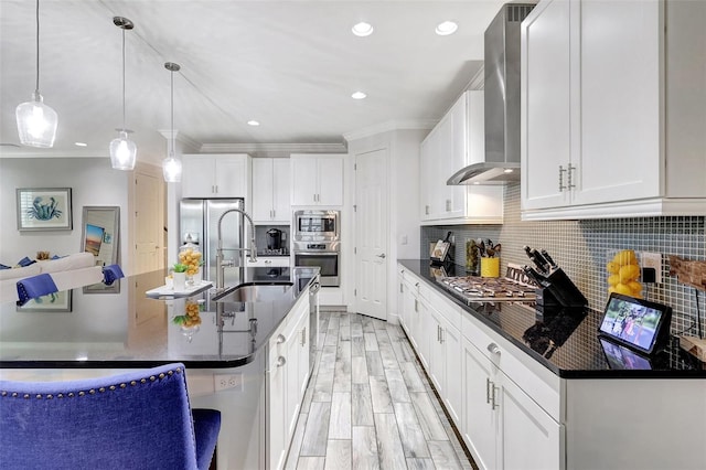 kitchen featuring wall chimney exhaust hood, white cabinetry, decorative light fixtures, and a kitchen island with sink