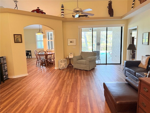 living room featuring wood-type flooring, ceiling fan, a high ceiling, and a healthy amount of sunlight