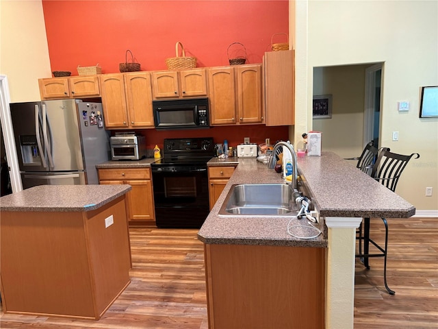 kitchen with sink, kitchen peninsula, black appliances, a kitchen breakfast bar, and light wood-type flooring