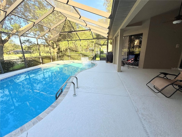 view of swimming pool with ceiling fan, glass enclosure, and a patio area