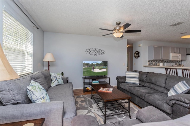 living room featuring ceiling fan, a textured ceiling, and light hardwood / wood-style floors