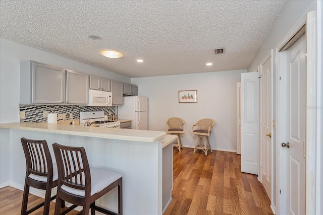 kitchen with white appliances, gray cabinetry, kitchen peninsula, and light hardwood / wood-style floors