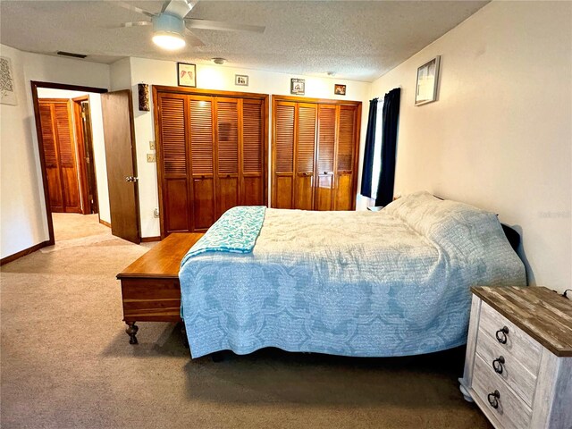 bedroom with two closets, a textured ceiling, light colored carpet, and ceiling fan