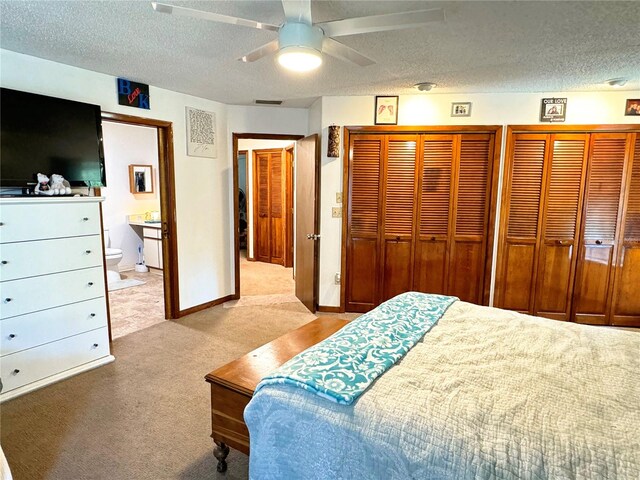 carpeted bedroom with a textured ceiling, ensuite bath, ceiling fan, and two closets