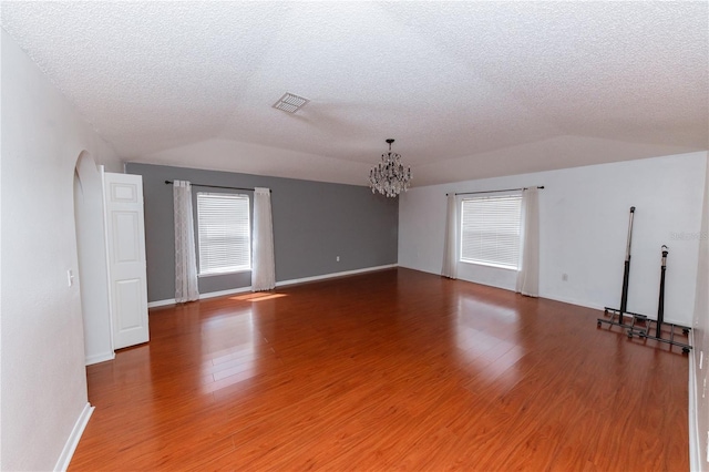 empty room featuring wood-type flooring, a textured ceiling, lofted ceiling, and a chandelier