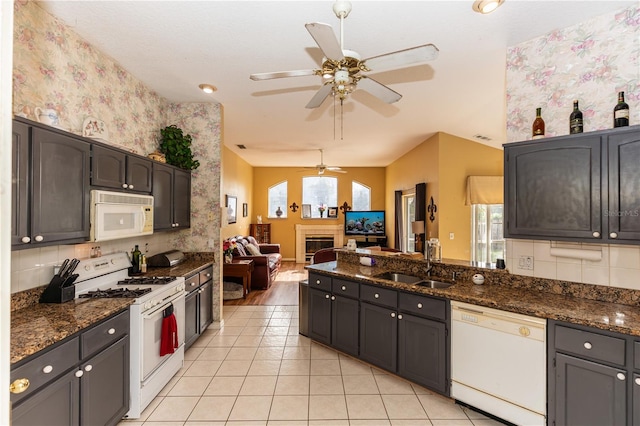 kitchen featuring light tile patterned flooring, lofted ceiling, sink, white appliances, and dark stone counters