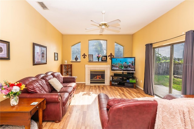 living room with ceiling fan, light wood-type flooring, a tiled fireplace, and a wealth of natural light