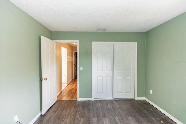 unfurnished bedroom with a textured ceiling, a closet, and dark hardwood / wood-style floors