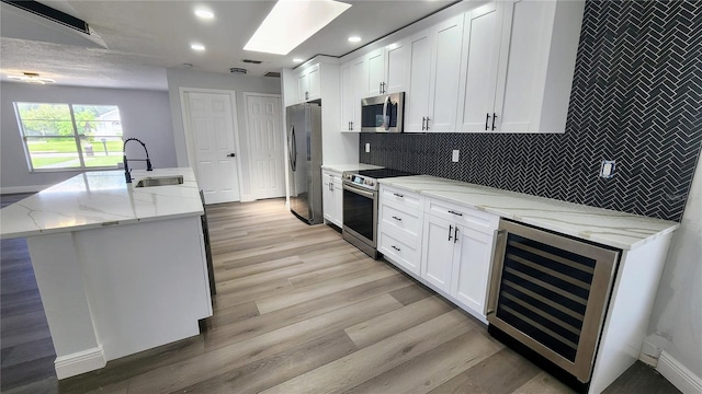 kitchen featuring wine cooler, appliances with stainless steel finishes, white cabinetry, light stone countertops, and sink