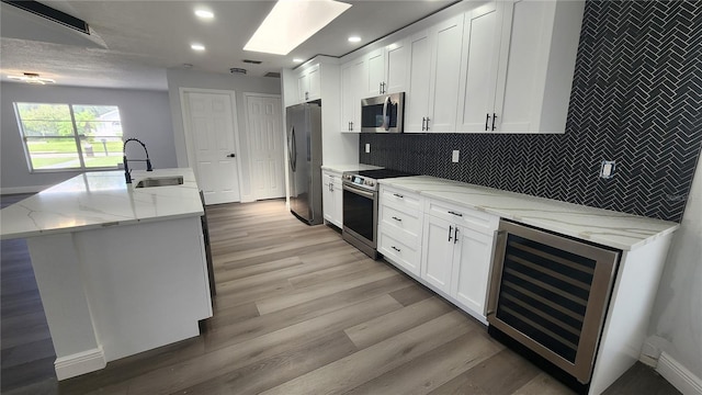 kitchen with white cabinets, beverage cooler, light stone countertops, sink, and stainless steel appliances