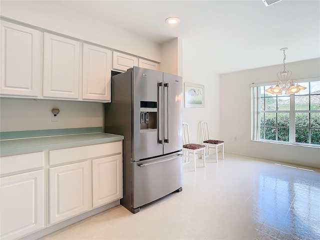 kitchen with an inviting chandelier, hanging light fixtures, stainless steel fridge, and white cabinetry