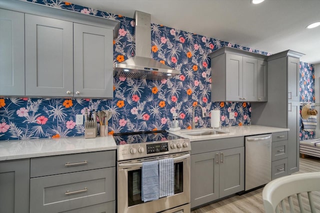 kitchen with light hardwood / wood-style floors, sink, wall chimney range hood, gray cabinetry, and appliances with stainless steel finishes