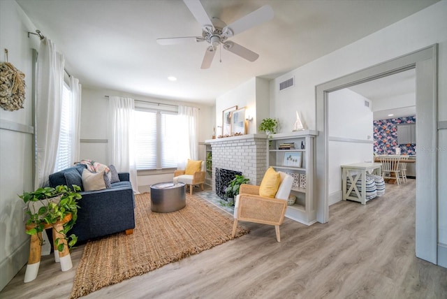 living room featuring a brick fireplace, light hardwood / wood-style floors, and ceiling fan